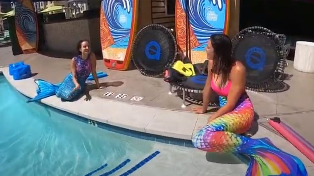two women wearing mermaid costumes near a pool